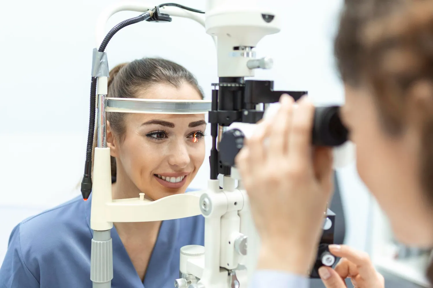 Smiling patient receiving an eye exam from an optometrist using a slit lamp microscope.