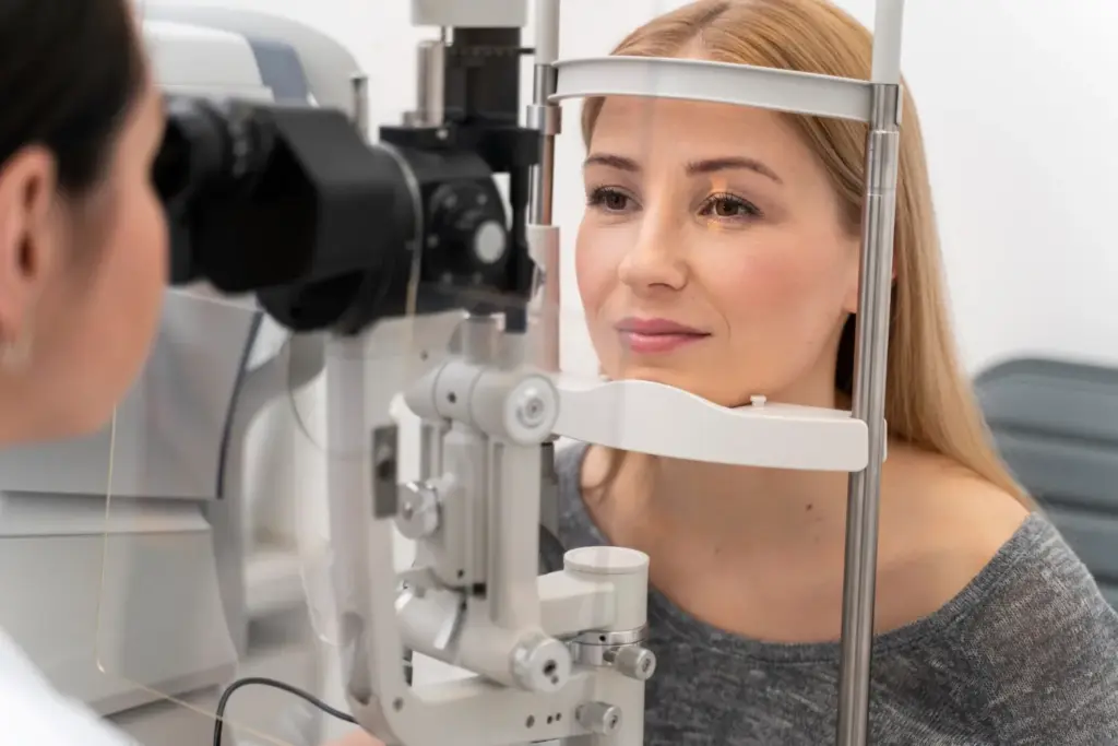 Woman receiving an eye exam, looking into a slit lamp operated by an optometrist.