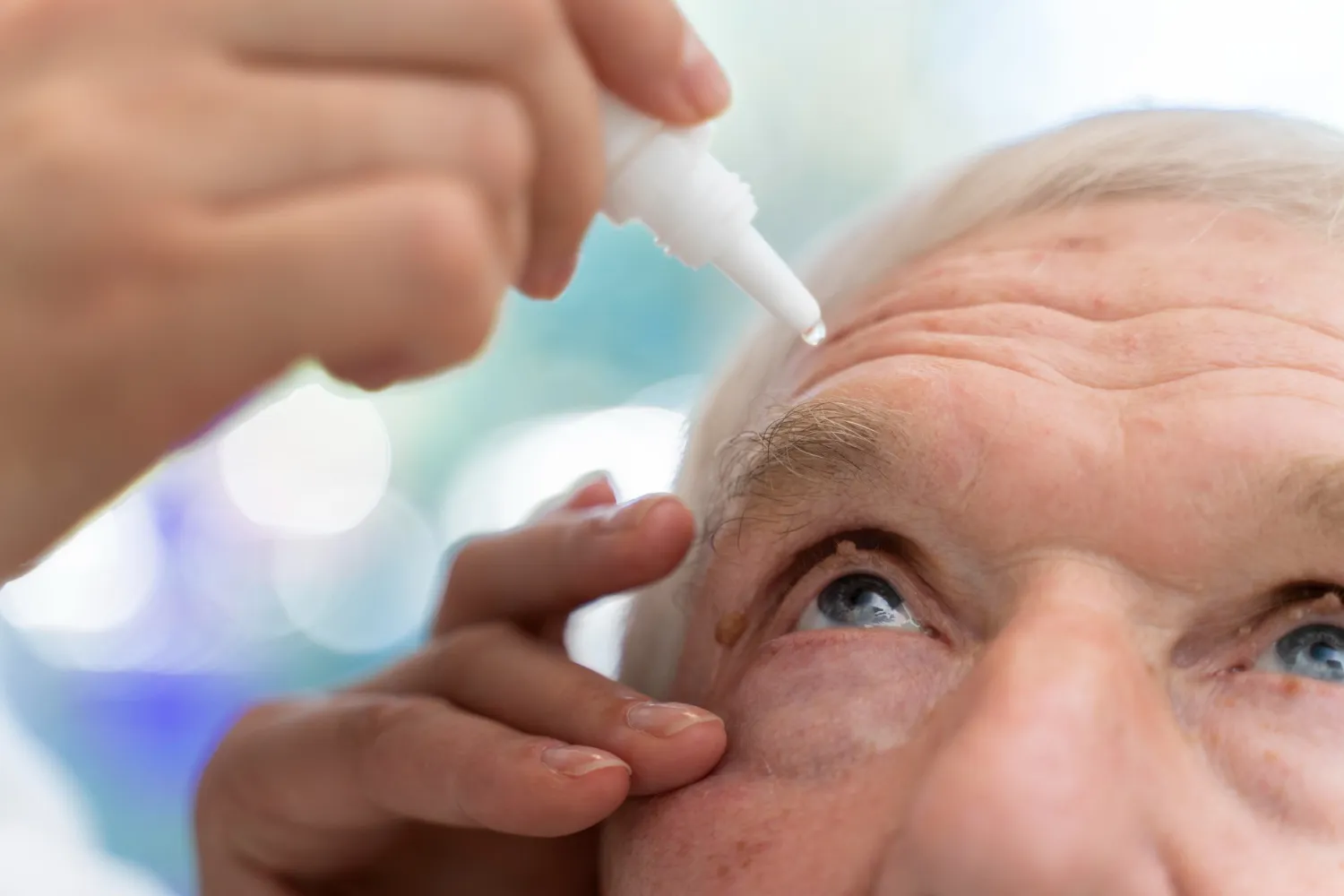 Close-up of a healthcare professional applying eye drops to an elderly man's eye.
