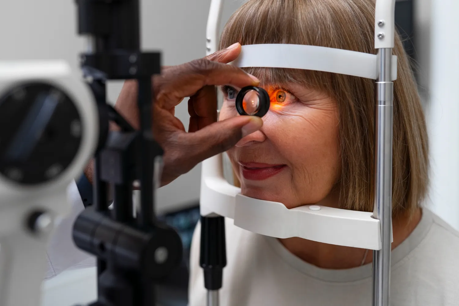Optometrist conducting an eye exam on a woman using specialized equipment; her eye is illuminated by a bright orange light.