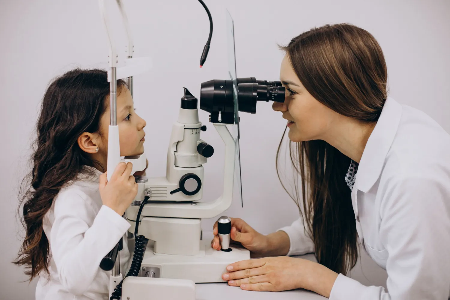 Ophthalmologist using a slit lamp microscope to examine a young girl's eyes during a pediatric vision check.