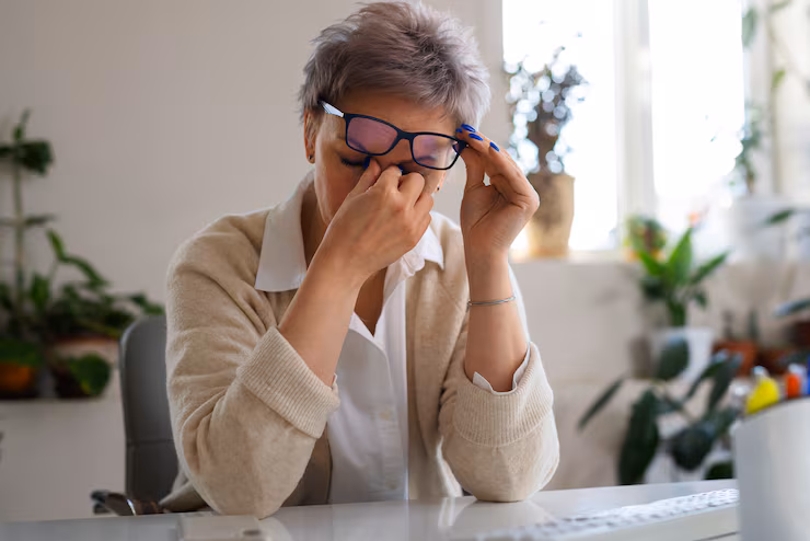 Woman sitting at a desk, pinching the bridge of her nose to relieve stress or eye strain.