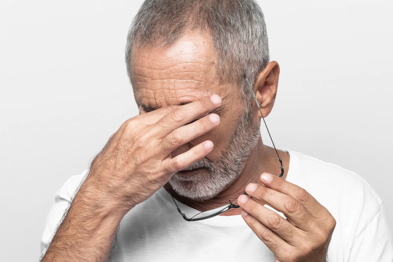 Senior man holding glasses and rubbing his strained or painful eyes.