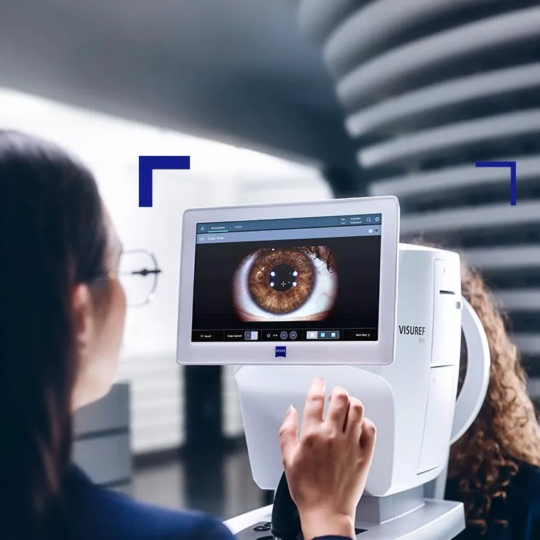 Ophthalmology technician operating advanced eye exam equipment, which displays a magnified, detailed view of a brown iris on the monitor.